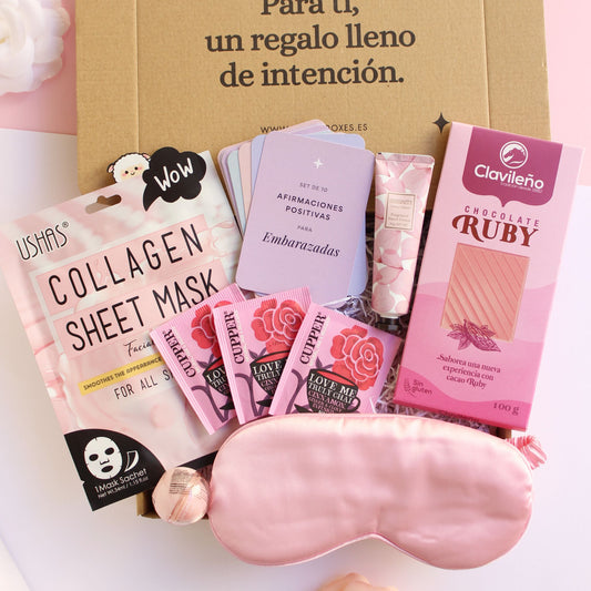 Caja regalo treat box para mujer embarazada que contiene mascarilla facial de colágeno, bálsamo para labios, antifaz satinado de color rosa, infusiones ecológicas, tableta de chocolate ruby, crema de manos con aroma de cereza y set de afirmaciones positivas para embarazadas.