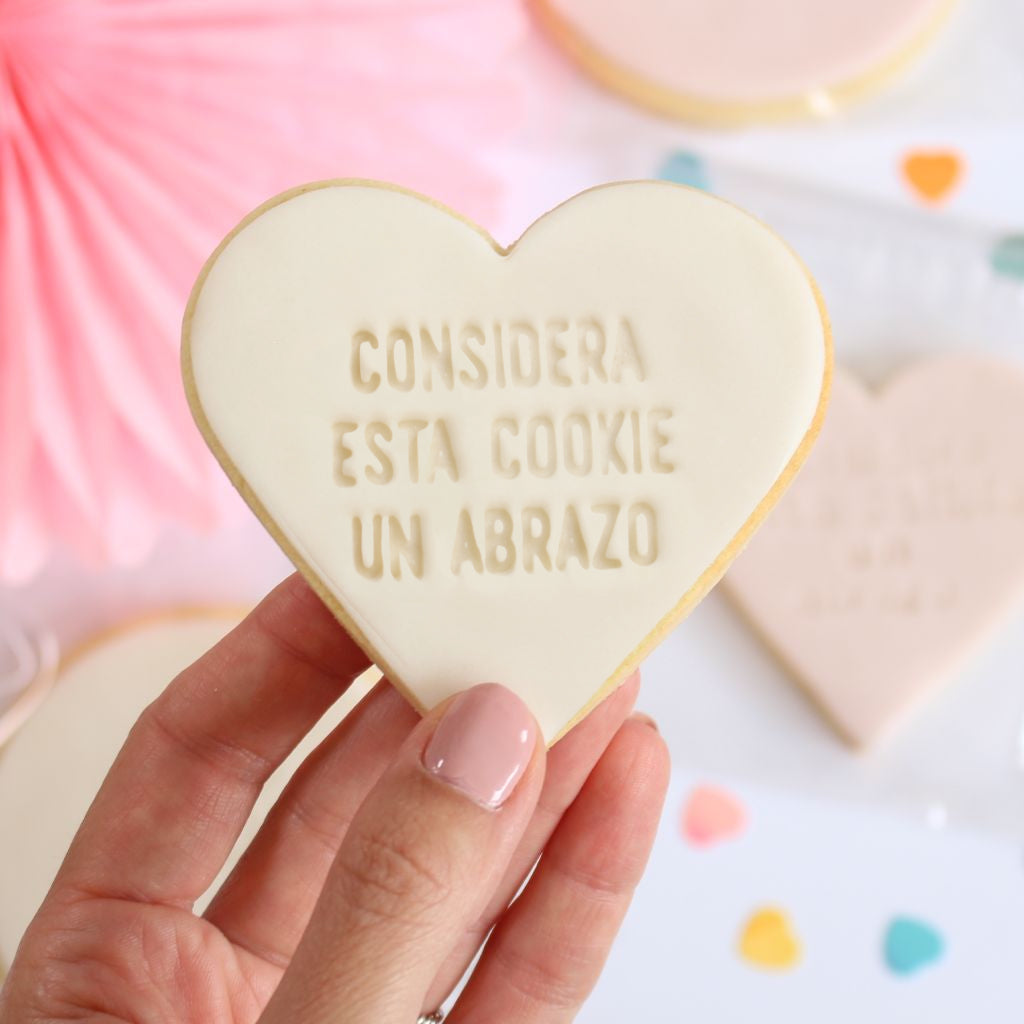 Galleta de mantequilla de color blanco con forma de corazón con la frase considera esta galleta un abrazo impresa