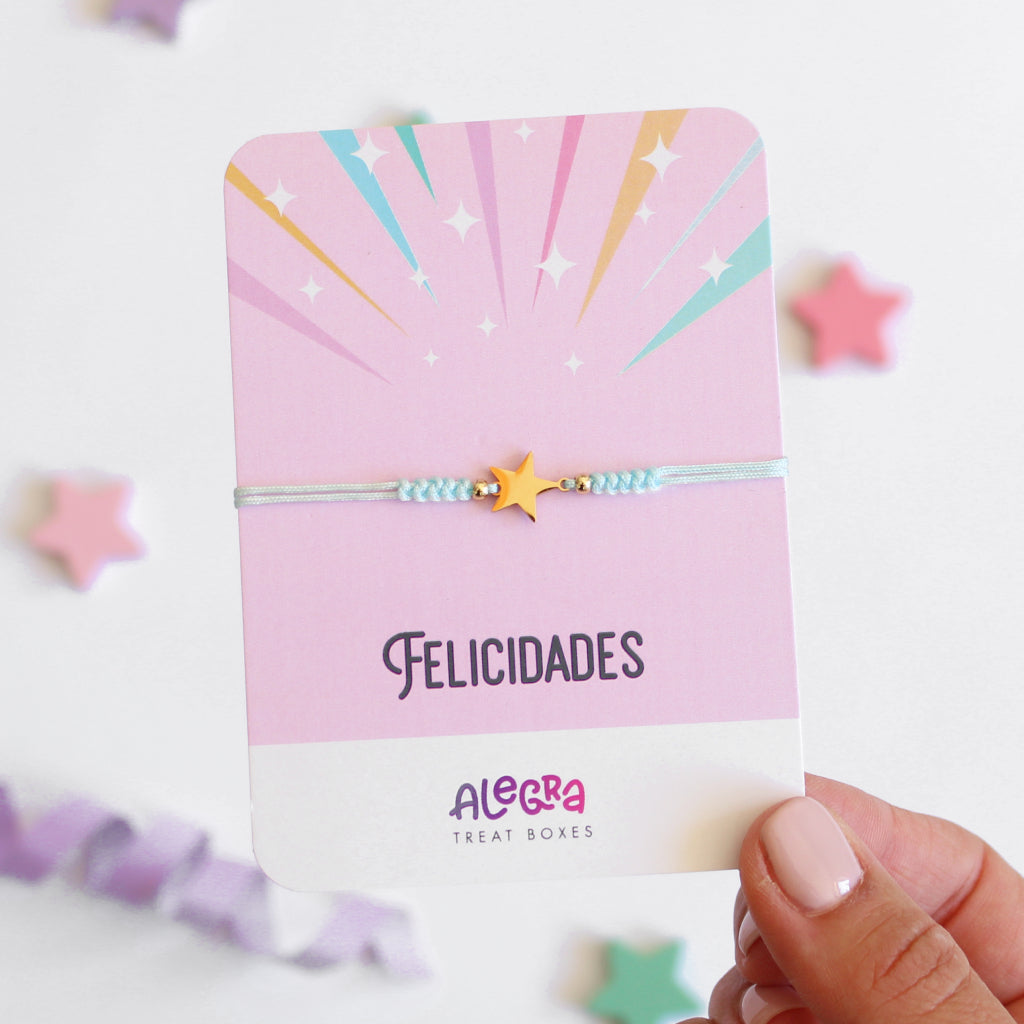 Pulsera de hilo color celeste con estrella de acero dorado en cartulina con la leyenda Felicidades