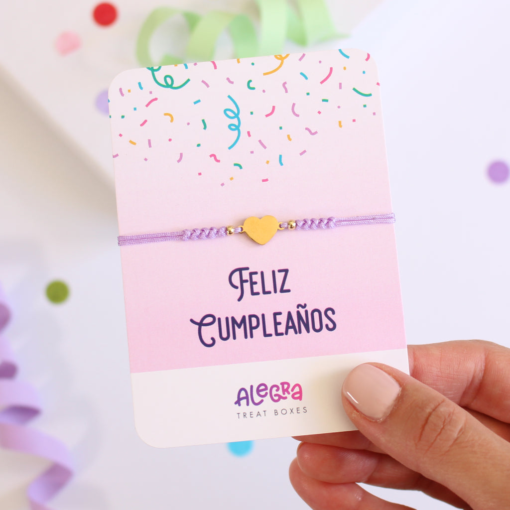 Pulsera de hilo color violeta con corazón de acero dorado en cartulina con la leyenda Feliz Cumpleaños