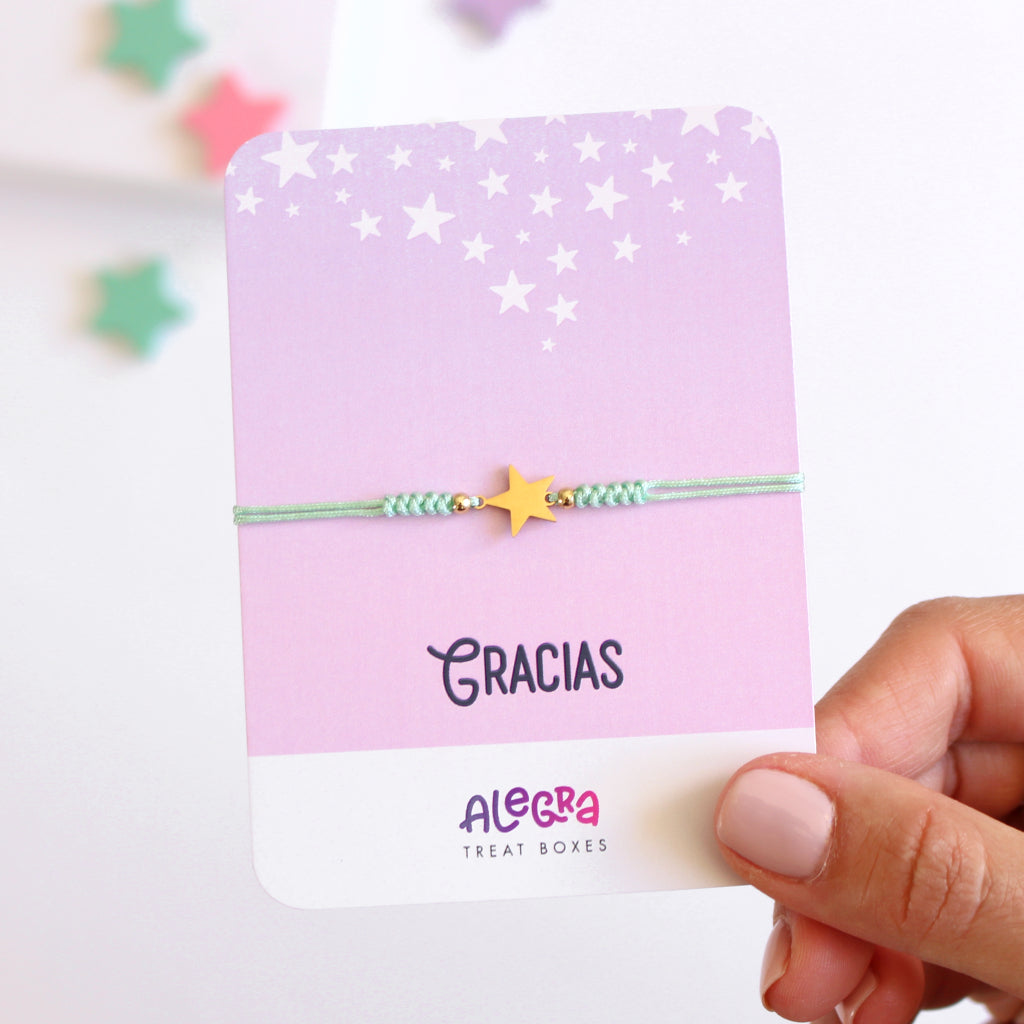 Pulsera de hilo color turquesa con estrella de acero dorado en cartulina con la leyenda Gracias