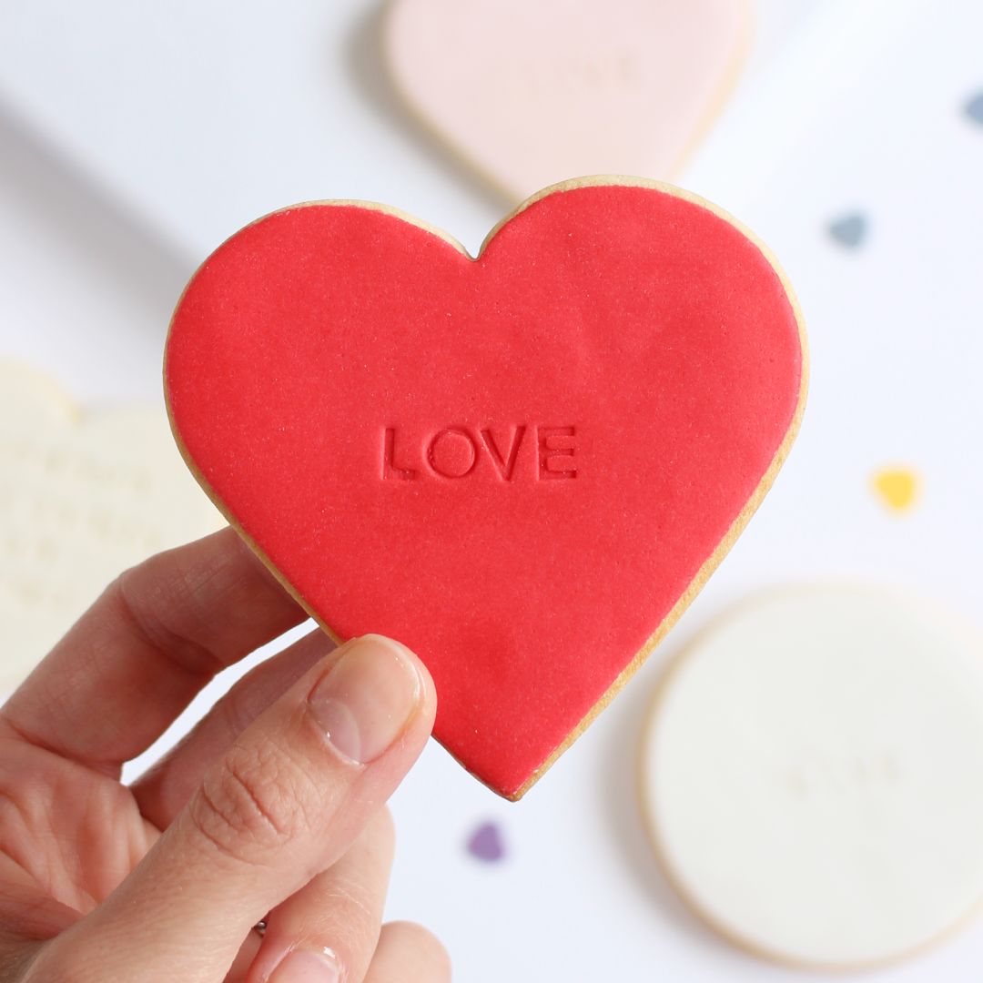 Galleta de mantequilla de color rojo con forma de corazón con la palabra love impresa