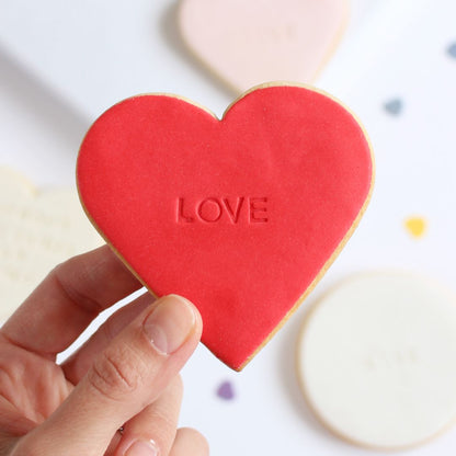 Galleta de mantequilla de color rojo con forma de corazón con la palabra love impresa