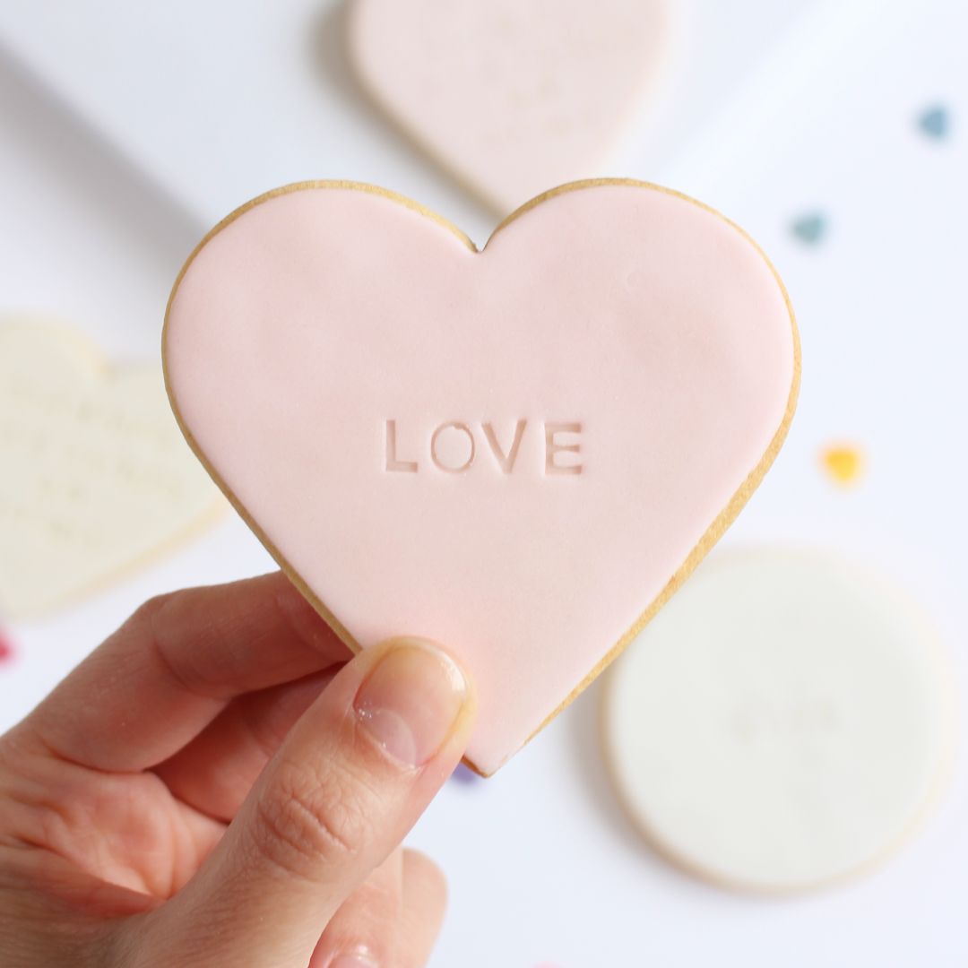 Galleta de mantequilla de color rosa  pálido con forma de corazón con la palabra love impresa