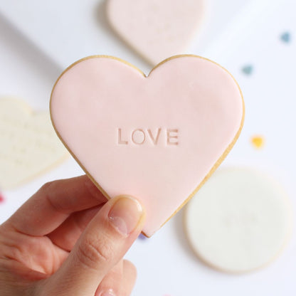 Galleta de mantequilla de color rosa  pálido con forma de corazón con la palabra love impresa