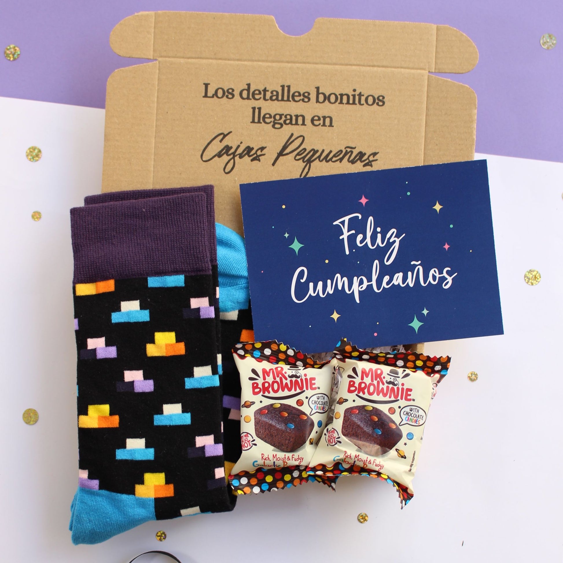 Mini caja regalo treat box de cumpleaños para hombre que contiene unos calcetines de color azul y negro con diseño de piezas de tetris en colores vivos, dos mini brownies de mr. brownie y una tarjeta de felicitación con el texto feliz cumpleaños
