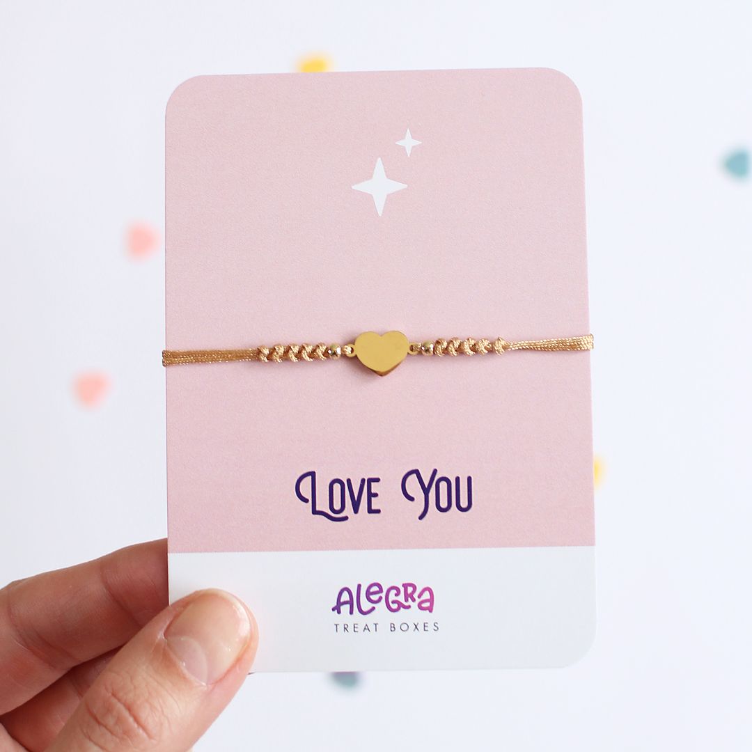 Pulsera de hilo color dorado con corazón de acero dorado en cartulina con la leyenda Love You