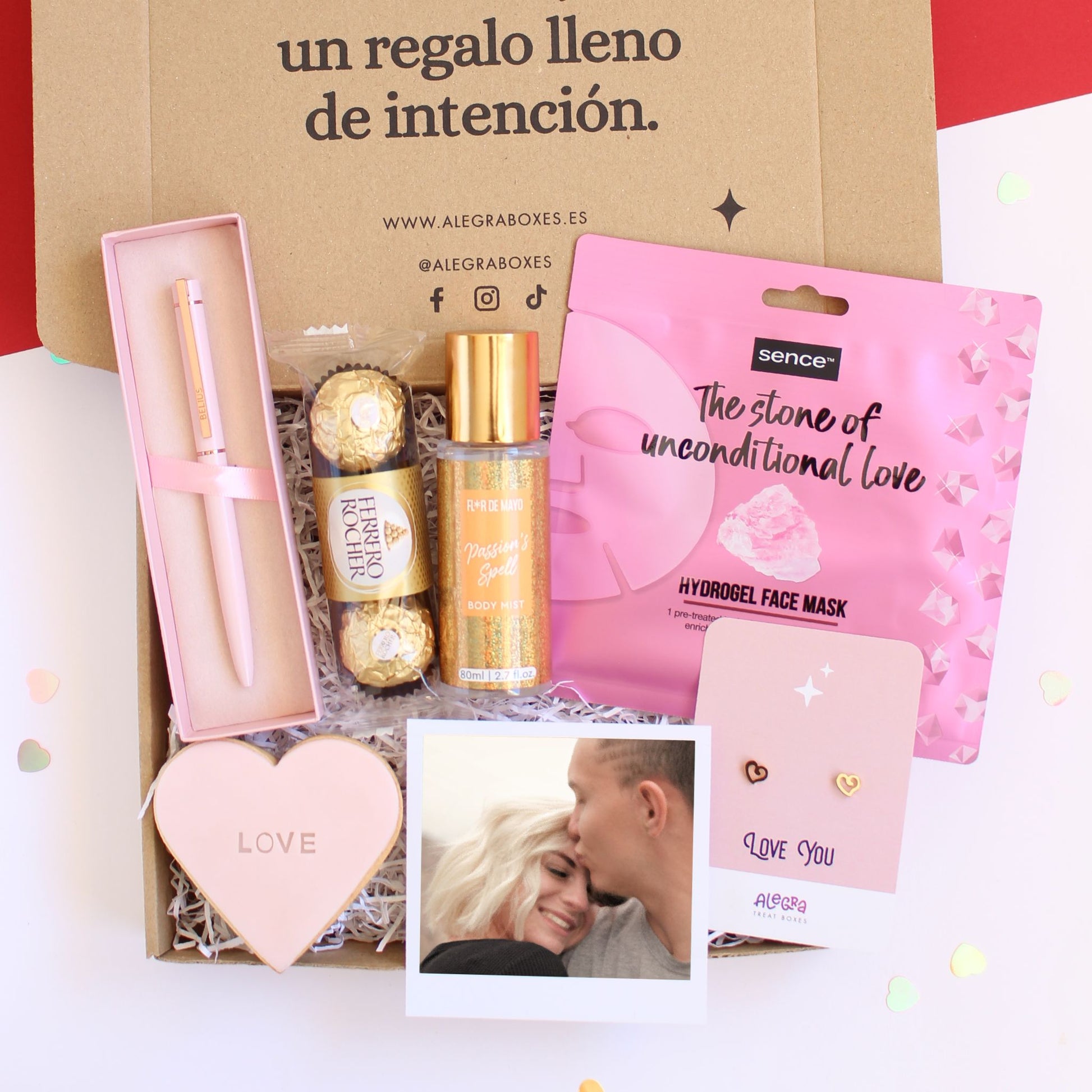 Caja regalo treat box para mujer que contiene galleta de mantequilla con forma de corazón, elegante bolígrafo de color rosa, tres bombones Ferero Rocher, bruma corporal, mascarilla facial de hidrogel, pendientes con forma de corazón de acero dorado y fotografía personalizada estilo Polaroid.